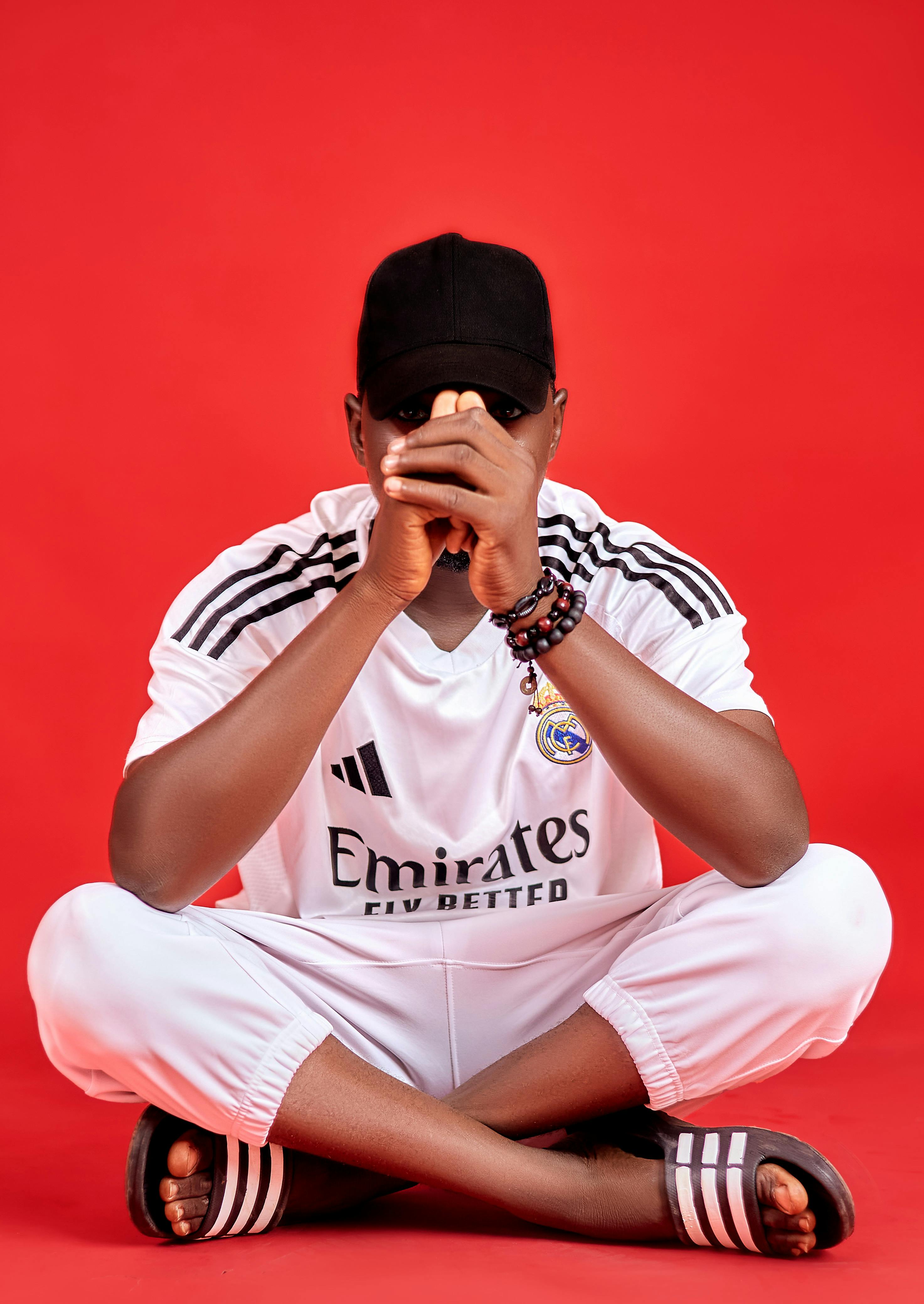 Man in white sportswear sitting on red background, showcasing casual style.