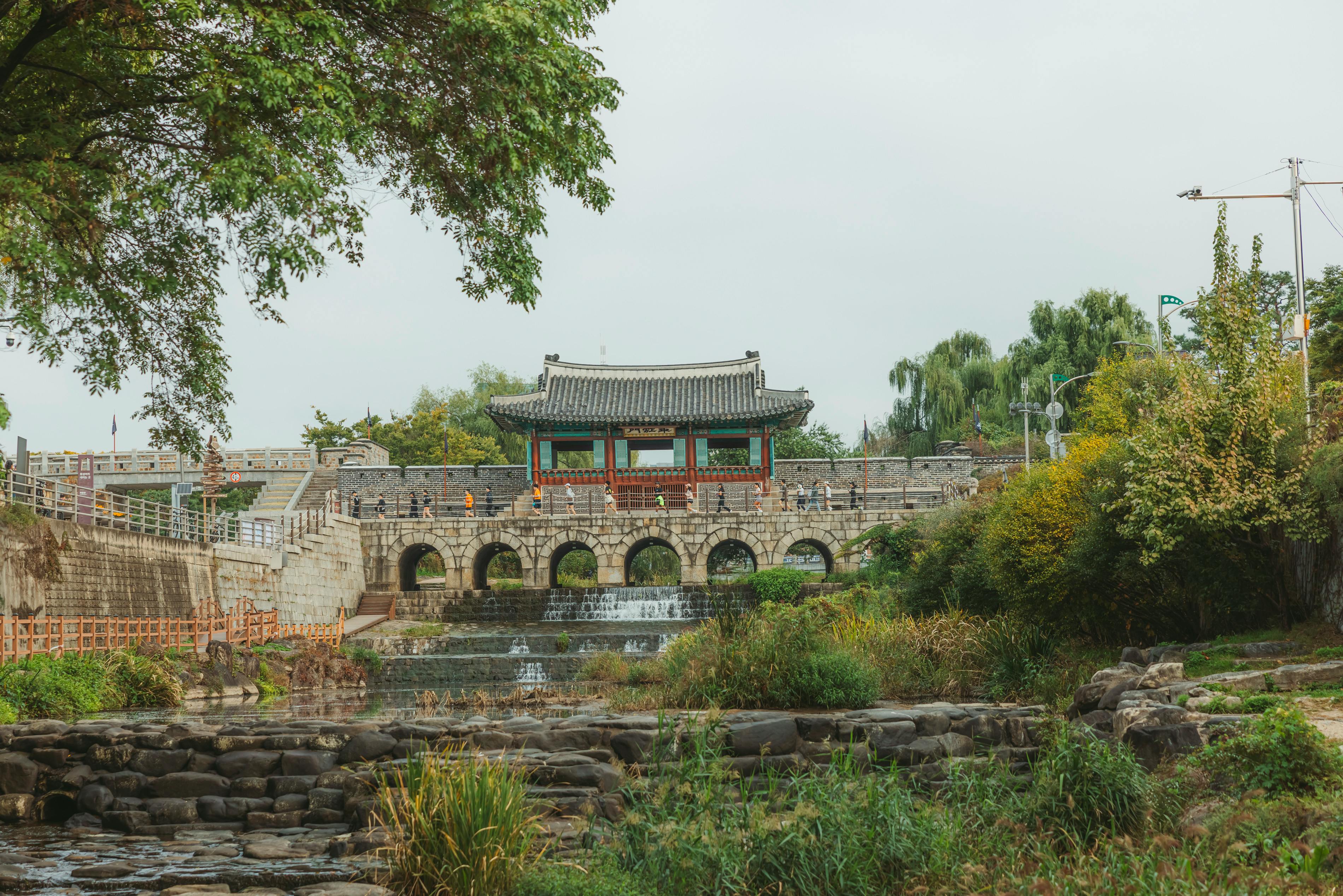 Historic Korean pavilion by a tranquil stream, surrounded by greenery.