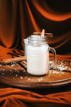 Cinnamon-infused rice milk in a glass jar on wooden tray with cozy background.