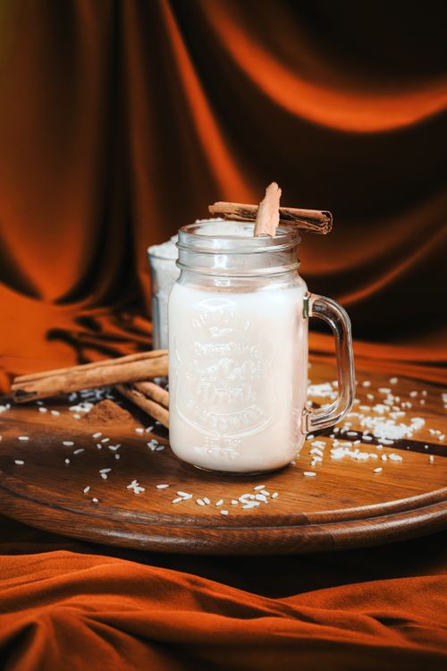 Free Cinnamon-infused rice milk in a glass jar on wooden tray with cozy background. Stock Photo