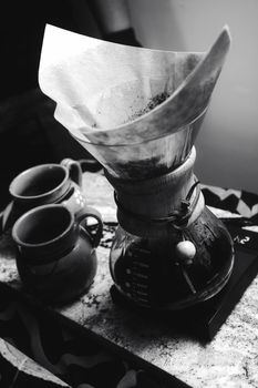 Stylish black and white shot of a coffee brewing setup with Chemex and cups.
