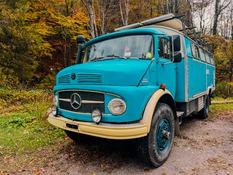 A classic blue truck parked in a vibrant autumn forest, showcasing nostalgia and nature's beauty.
