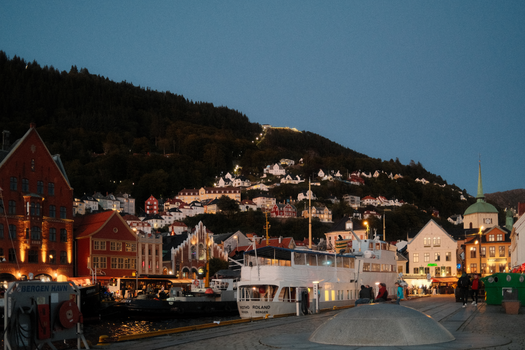 Scenic evening view of Bergen's iconic Bryggen waterfront with lit buildings and boats.