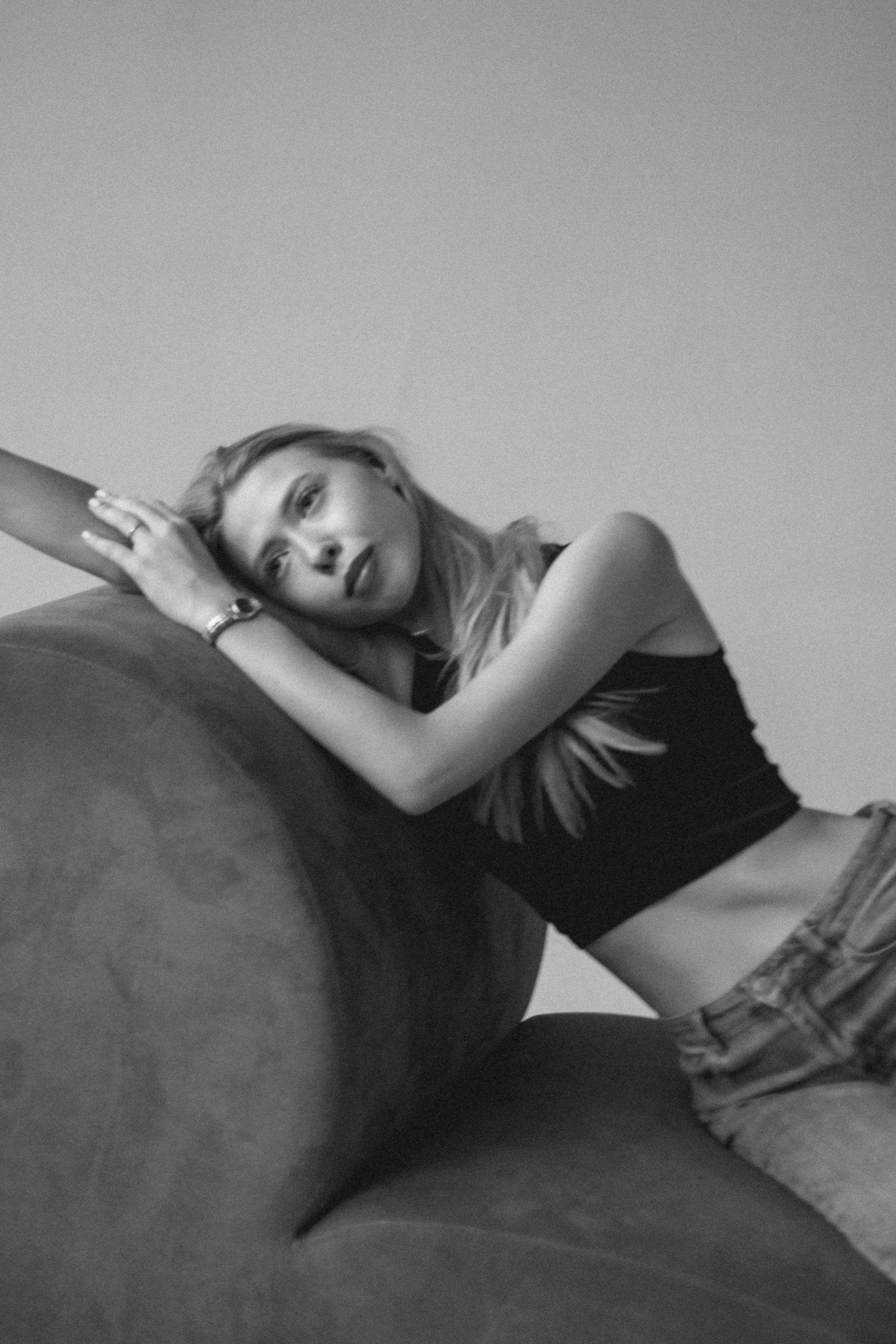 Black-and-white portrait of a woman leaning on a curved sofa in a relaxed pose.