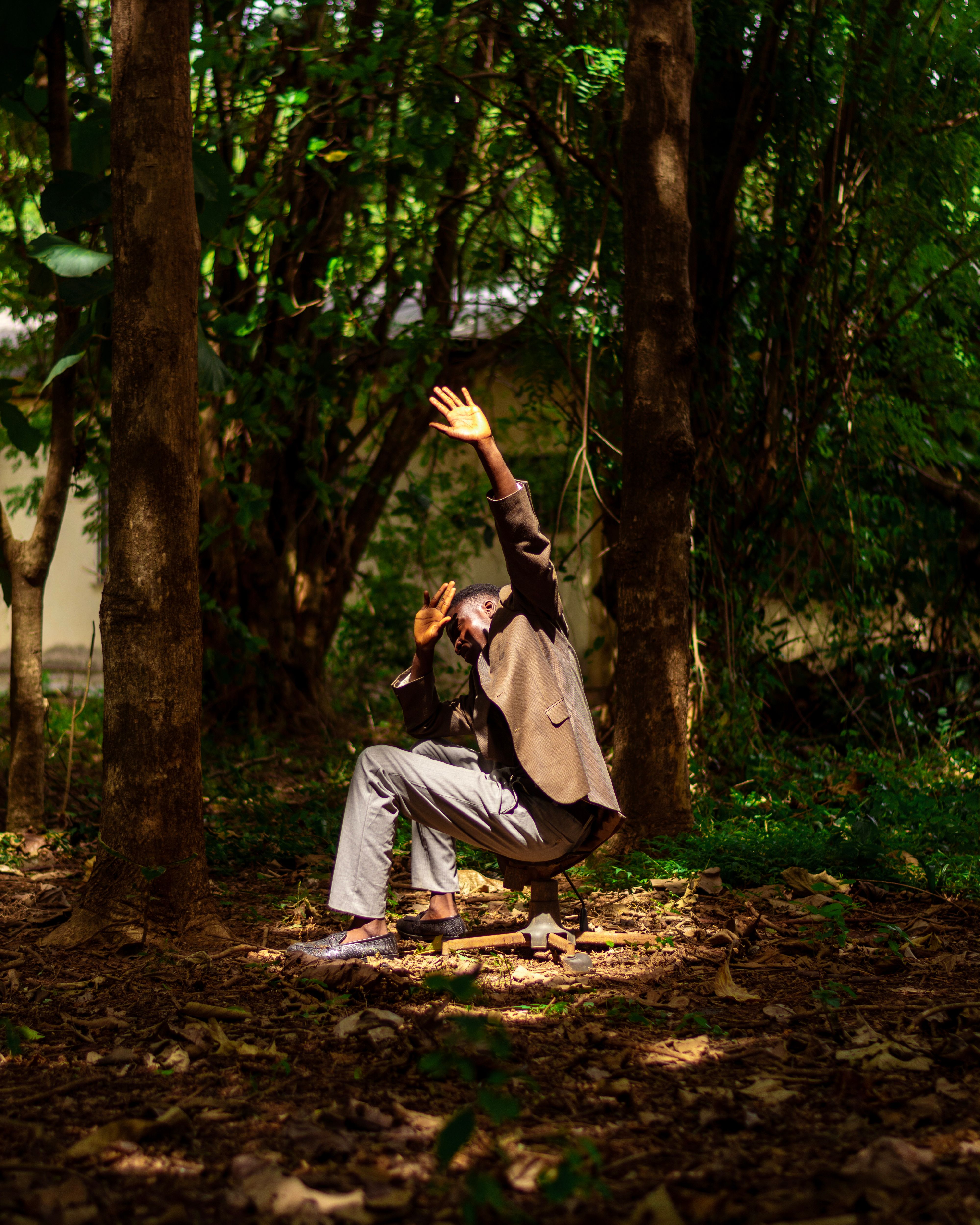 African man in a suit sits under trees in a forest in Ado Ekiti, Nigeria.