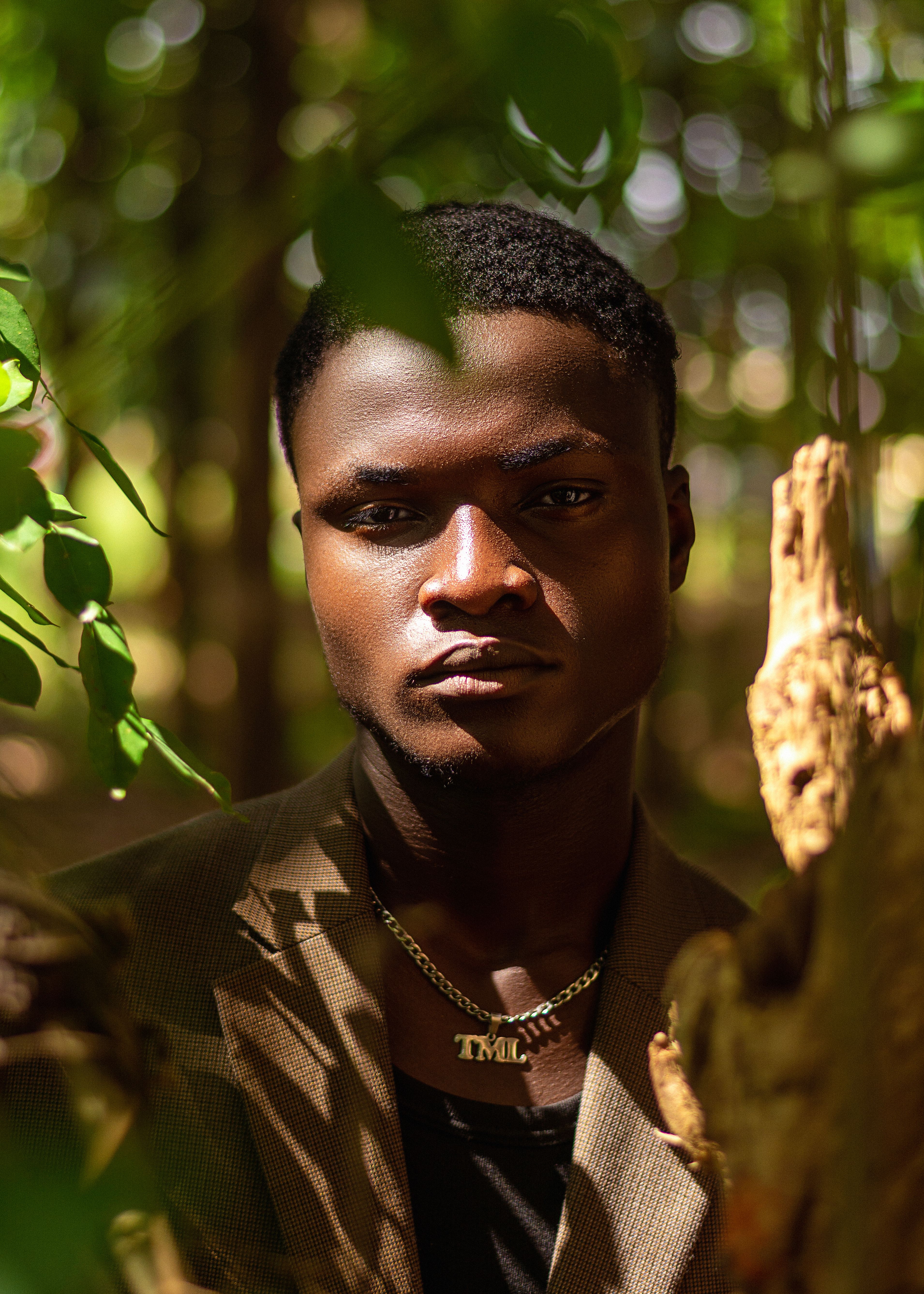 A contemplative young man stands amidst the vibrant greens of a forest setting.