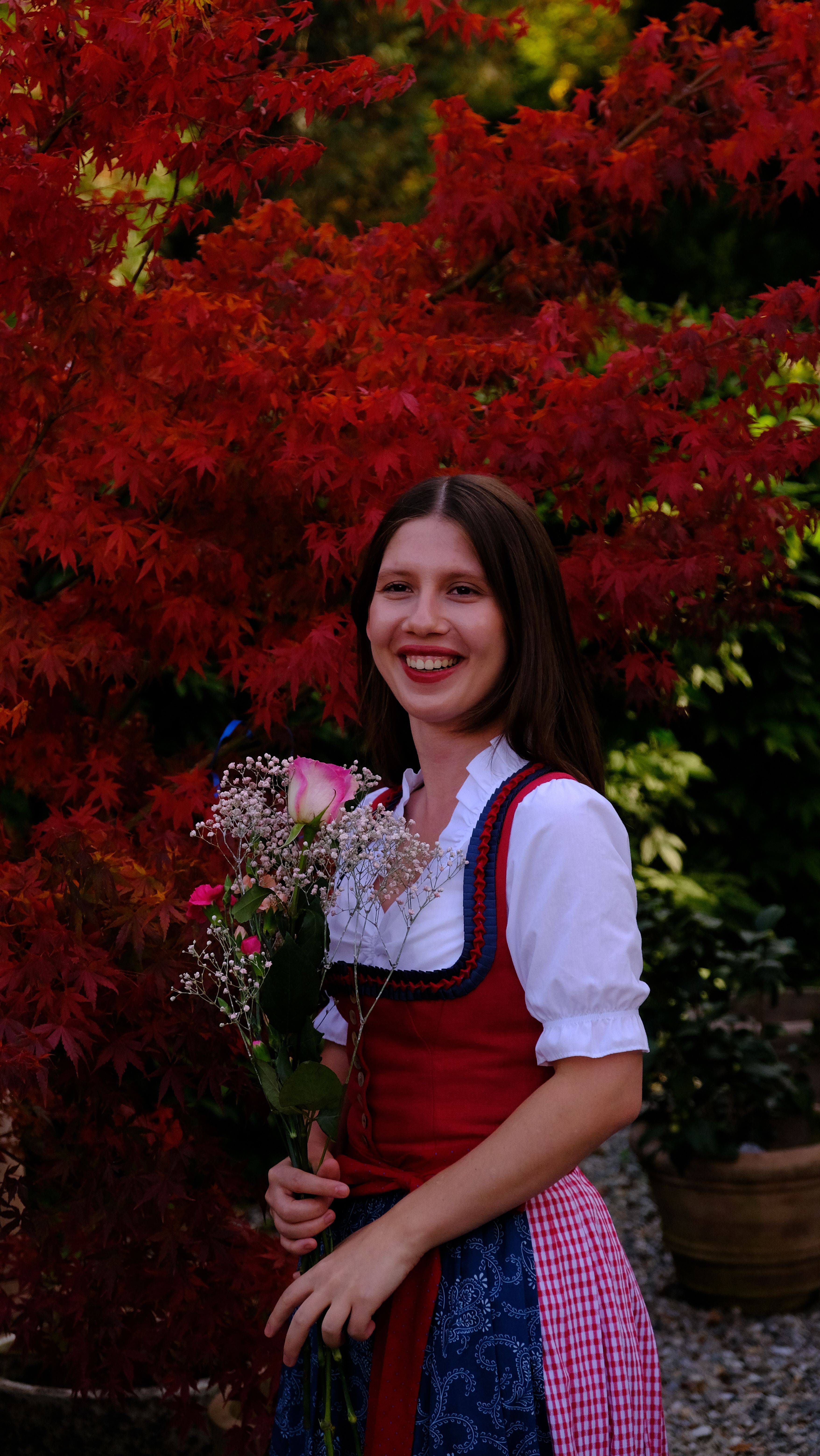 Woman in Dirndl with a bouquet, posing in an autumn garden, Graz, Austria.