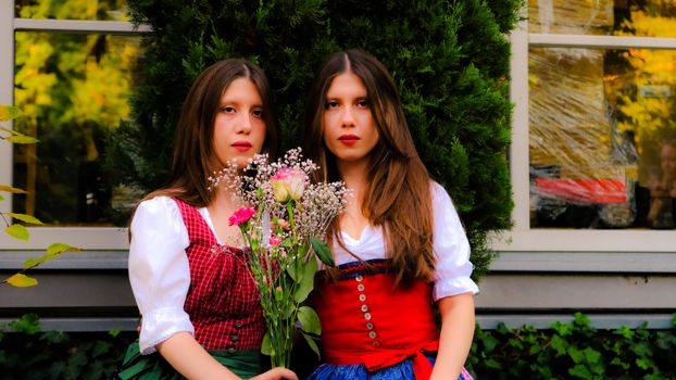 Two women in Austrian dirndl dresses holding flowers in a rustic setting, capturing autumn ambiance in Graz.