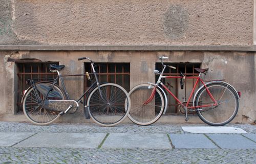 Free Two classic bicycles leaning against a textured urban wall on a cobblestone street. Stock Photo
