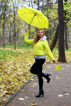 Smiling woman in autumn park holding a yellow umbrella and leaf.