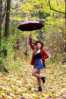 Young woman in autumn forest posing playfully with a red umbrella.