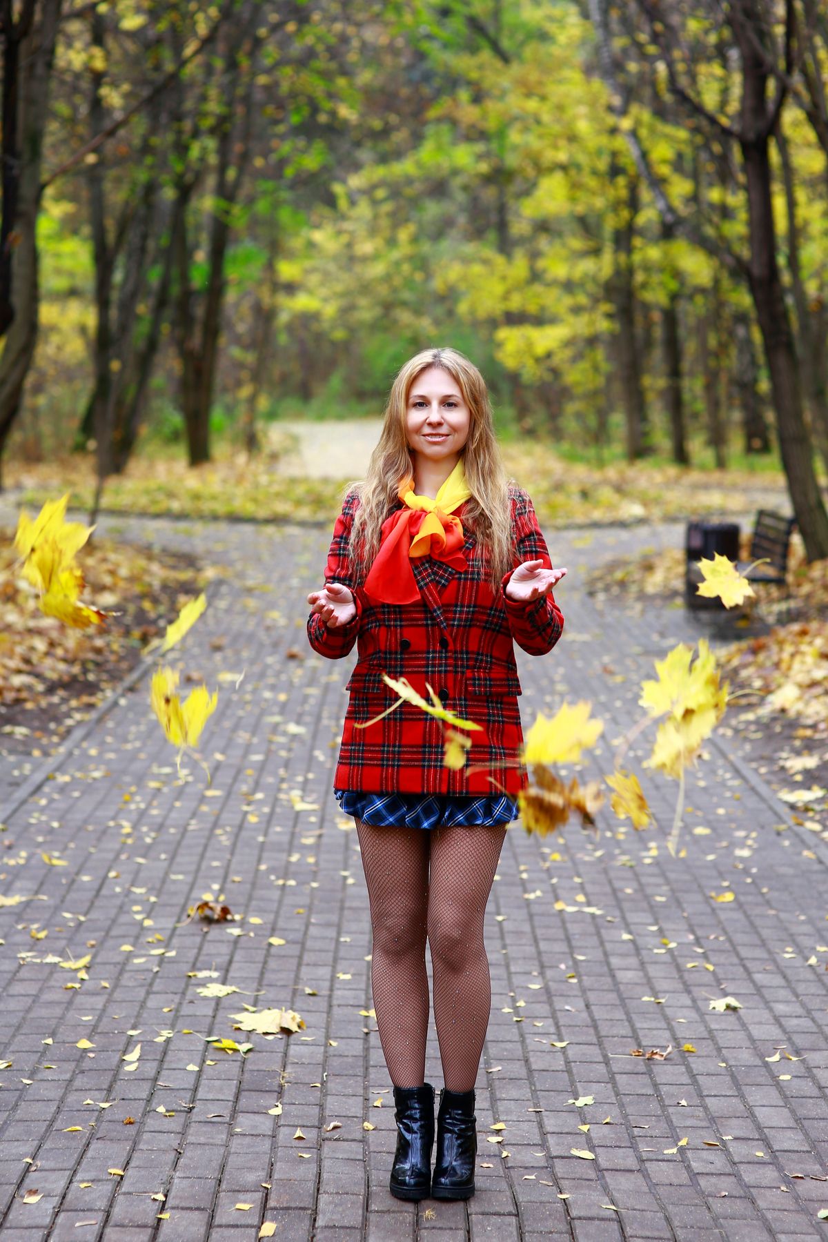 Young woman in a red coat plays with autumn leaves in a vibrant park setting.