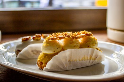 Delicious gourmet eclairs topped with cream and nuts on a white plate.