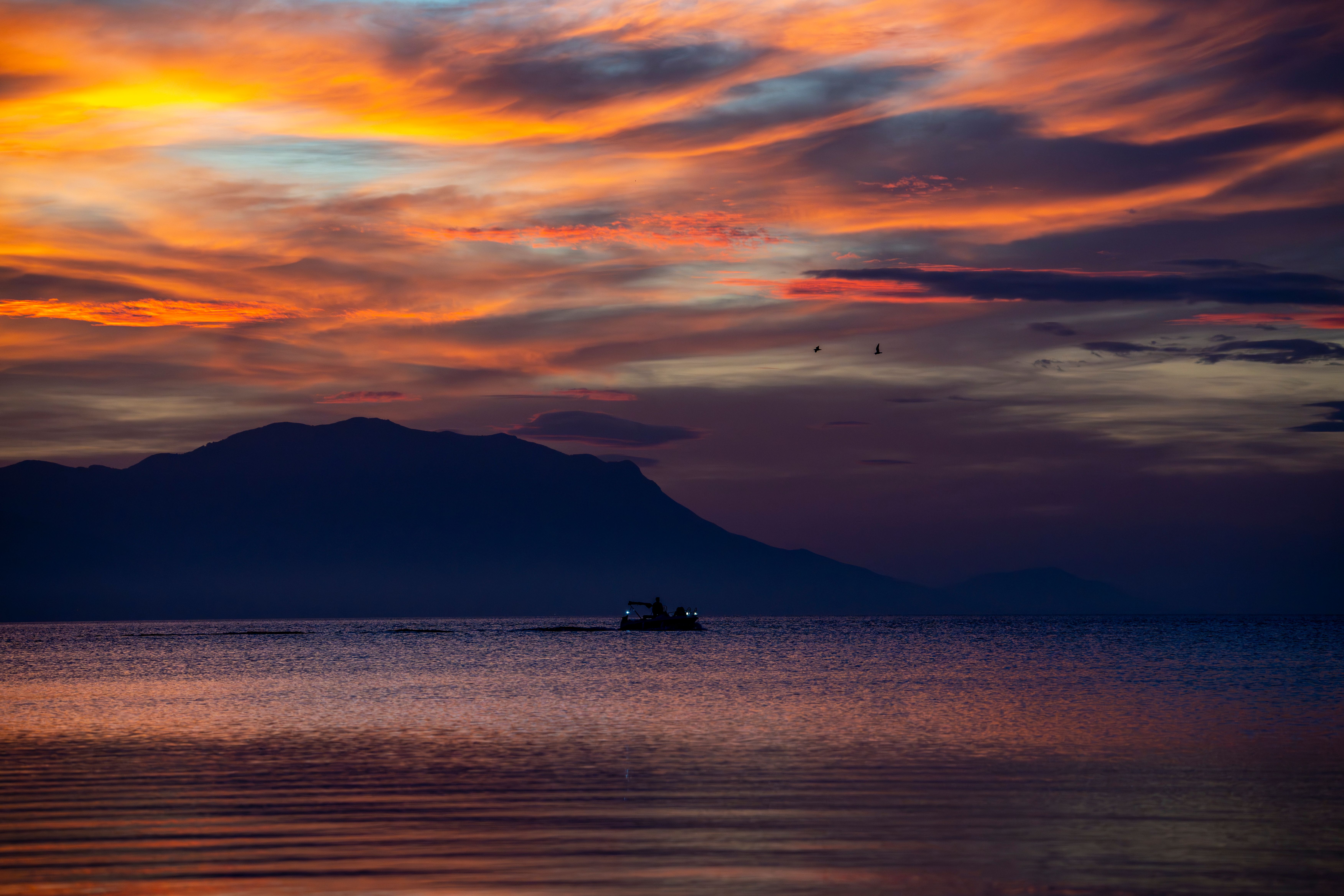 Dramatic Sunset Over Tranquil Sea with Silhouetted Boat · Free Stock Photo