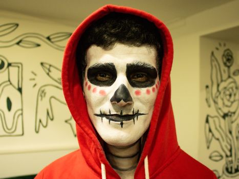 Young adult with Day of the Dead face paint and red hoodie indoors.