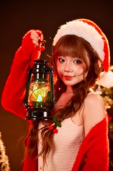 Young woman in Santa hat holding a lantern, exuding holiday cheer with warm lighting.