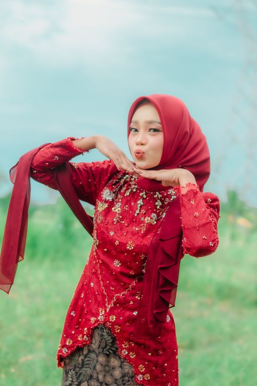 Free A woman in a red hijab and traditional dress posing playfully outdoors. Stock Photo