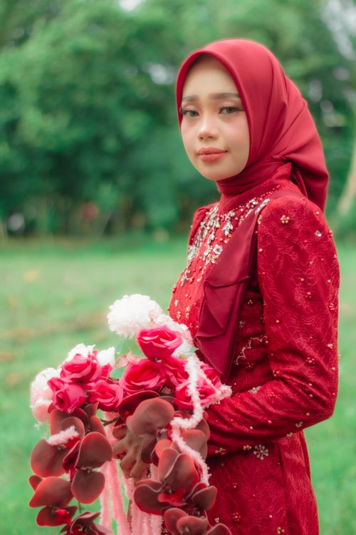 Free Woman in red dress and hijab holding a floral bouquet outdoors. Stock Photo