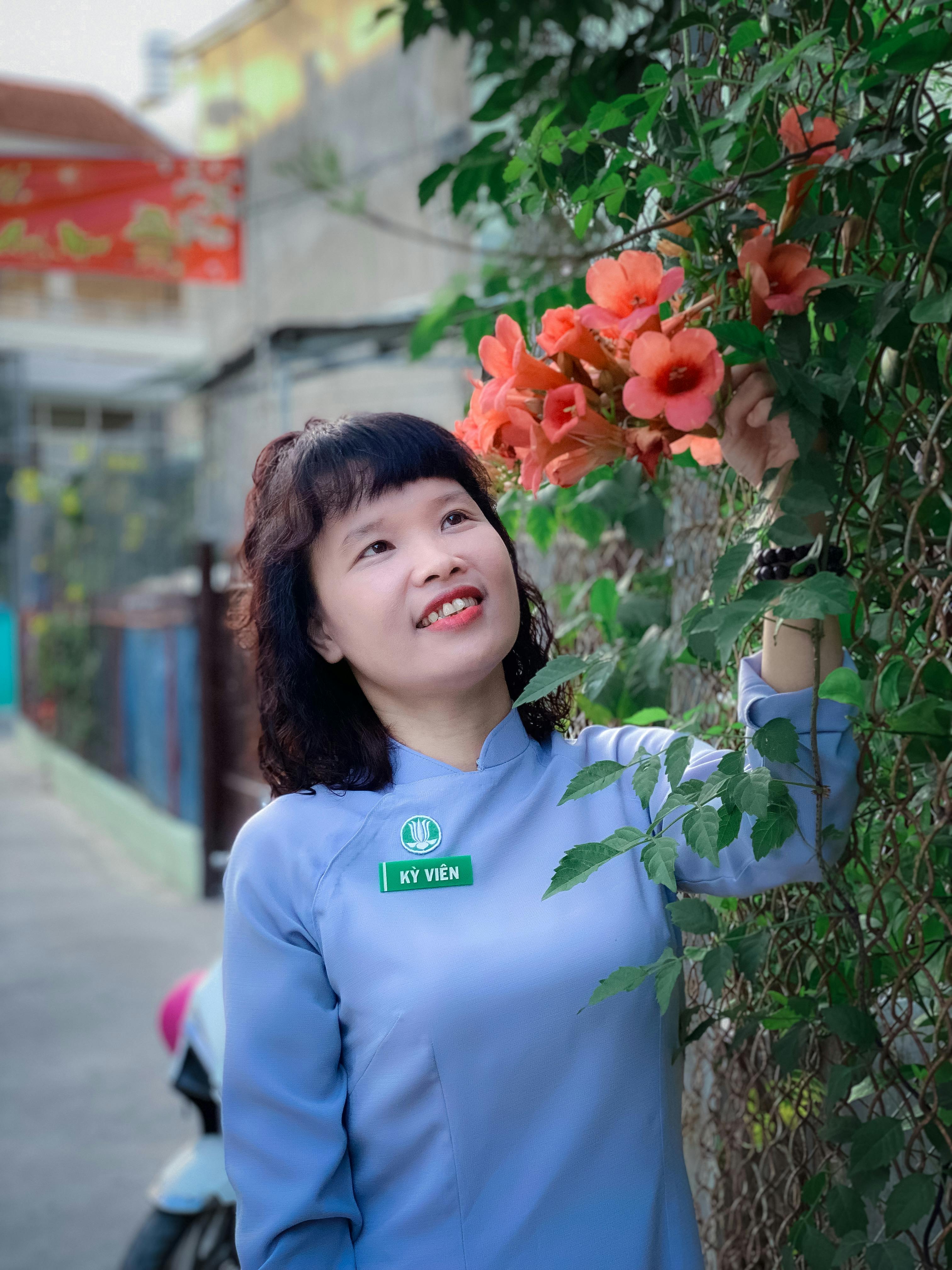 A cheerful woman in blue enjoys vibrant orange flowers on a sunny day.