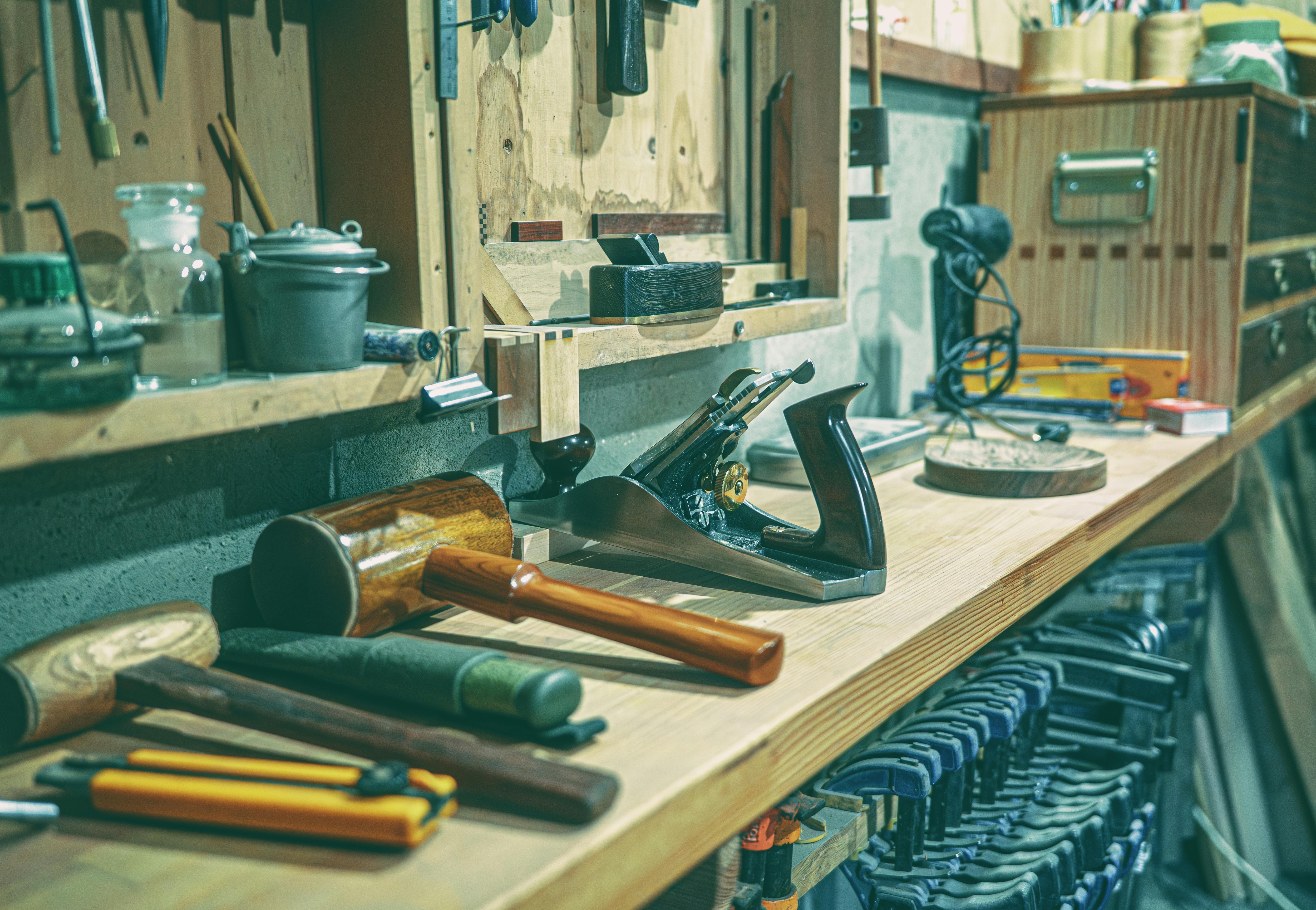 Workbench with tools: mallet, plane, clamps, and hand tools on a wooden surface in a workshop.