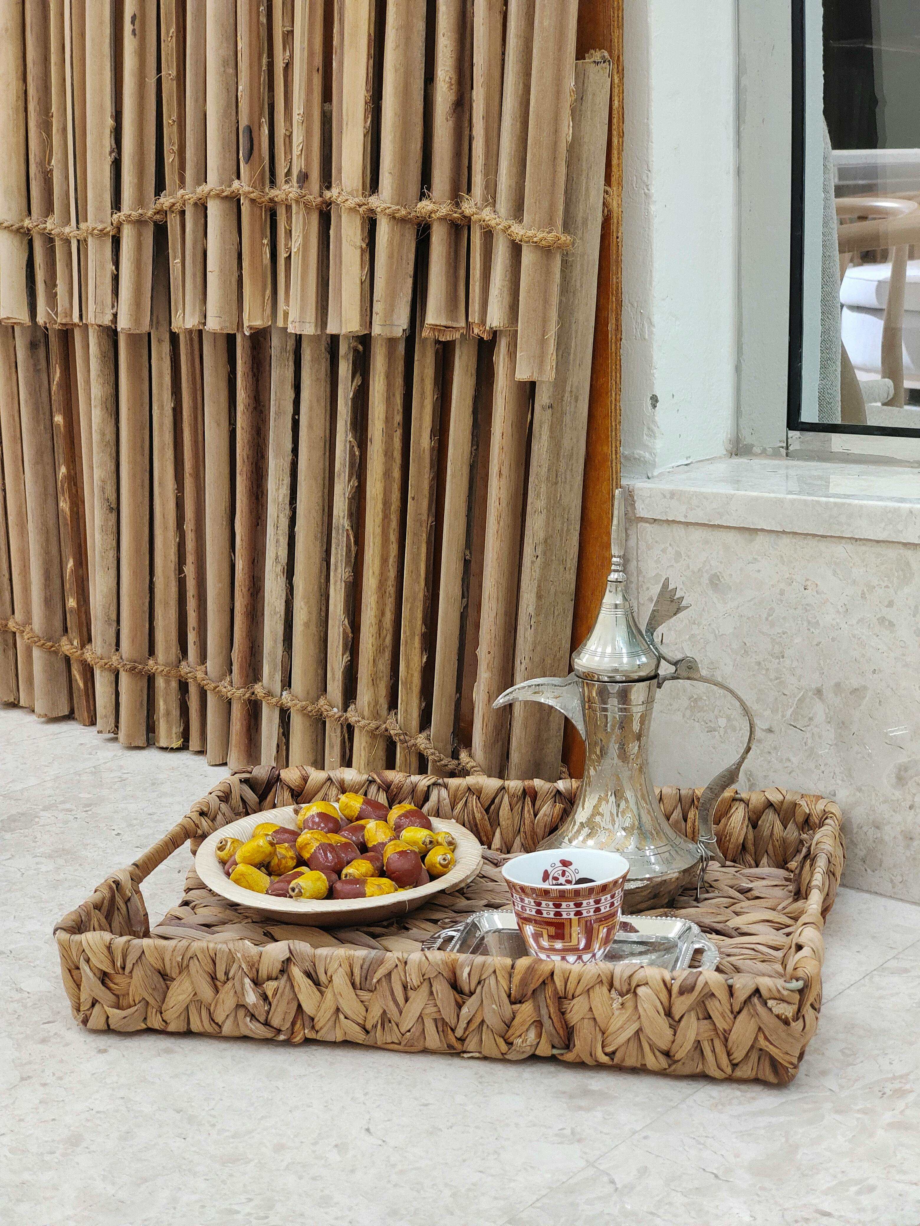 A woven platter with traditional Arabic coffee, dates, and a Dallah pot.