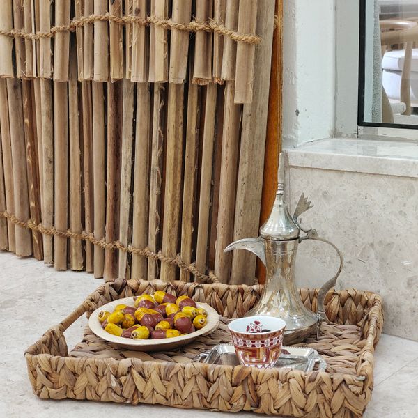 A woven platter with traditional Arabic coffee, dates, and a Dallah pot.