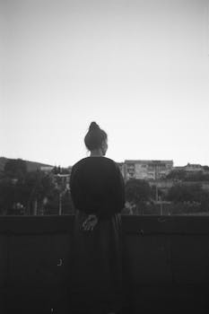 Black and white image of a woman viewing a cityscape from a rooftop.