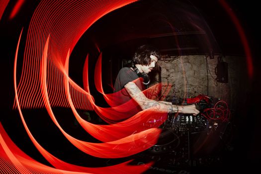 A DJ performing in a dimly lit club with captivating red light trails and mixing equipment.