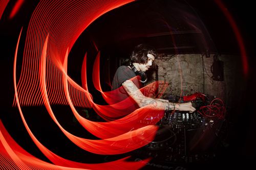 Free A DJ performing in a dimly lit club with captivating red light trails and mixing equipment. Stock Photo