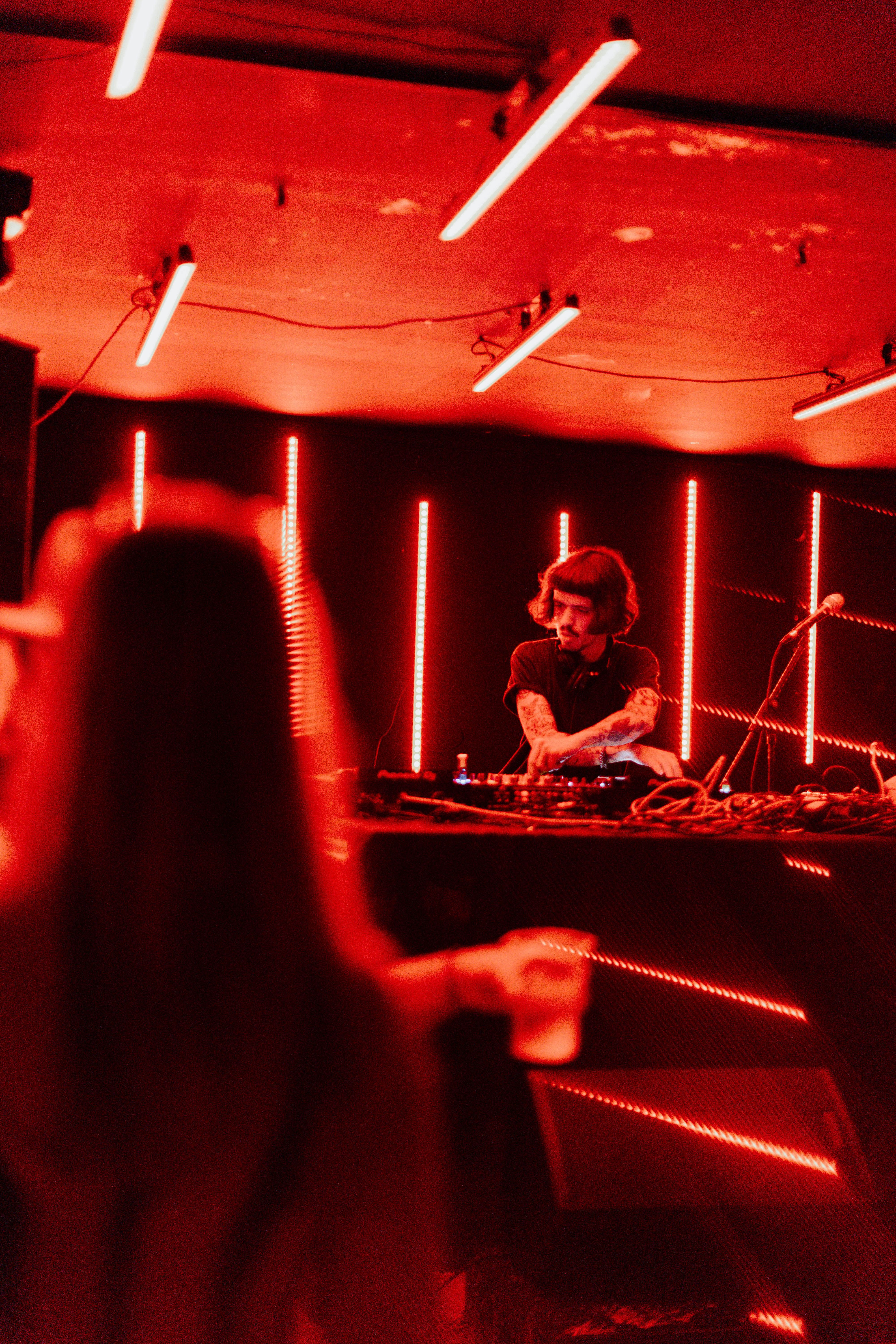 Dynamic nightclub atmosphere with a DJ playing music under red neon lights.