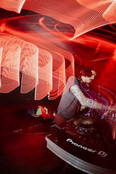 Dynamic photo of a DJ mixing music with vibrant red light trails and club atmosphere.