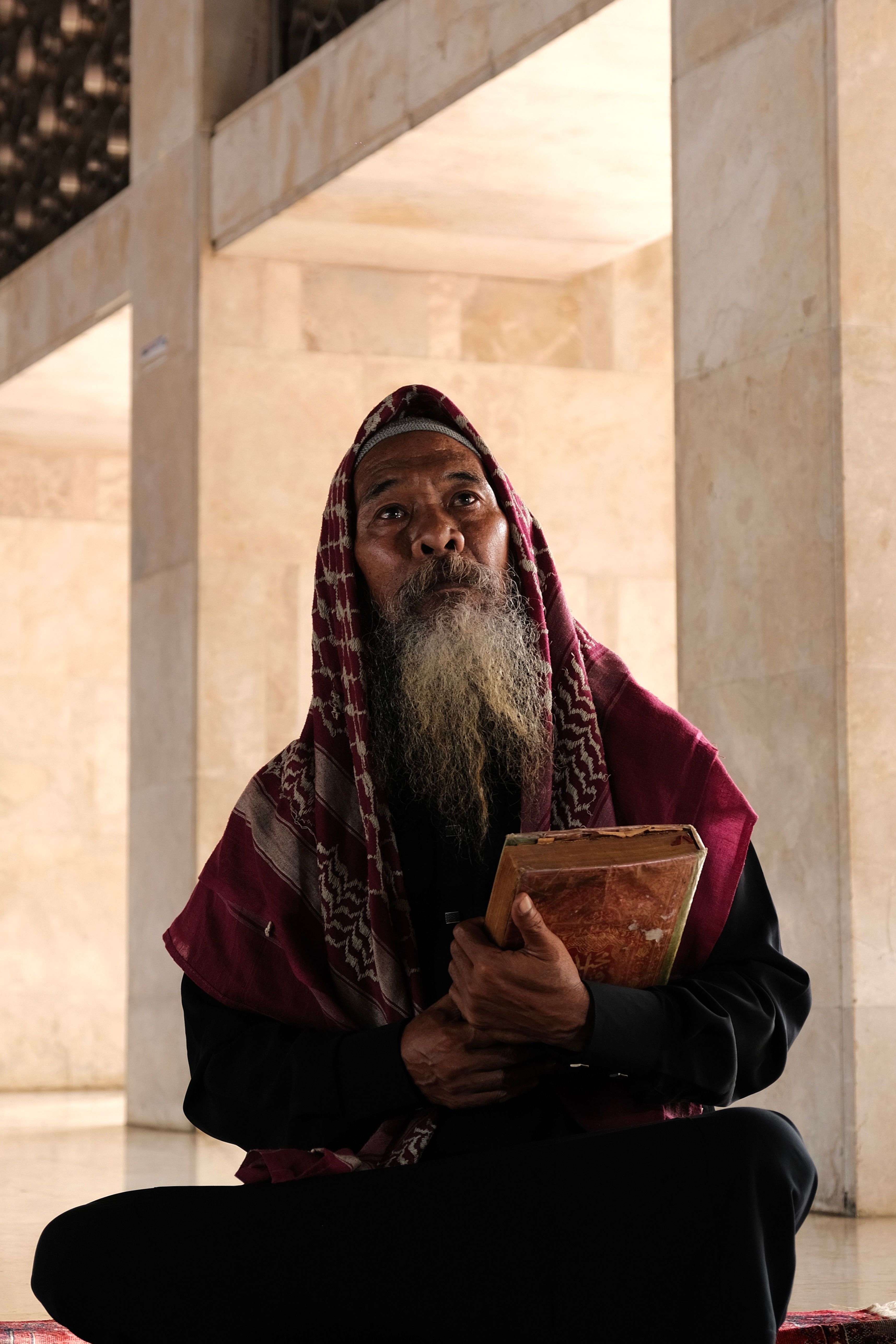 An elderly man sitting in a mosque in Jakarta, Indonesia, engaged in Islamic prayer.