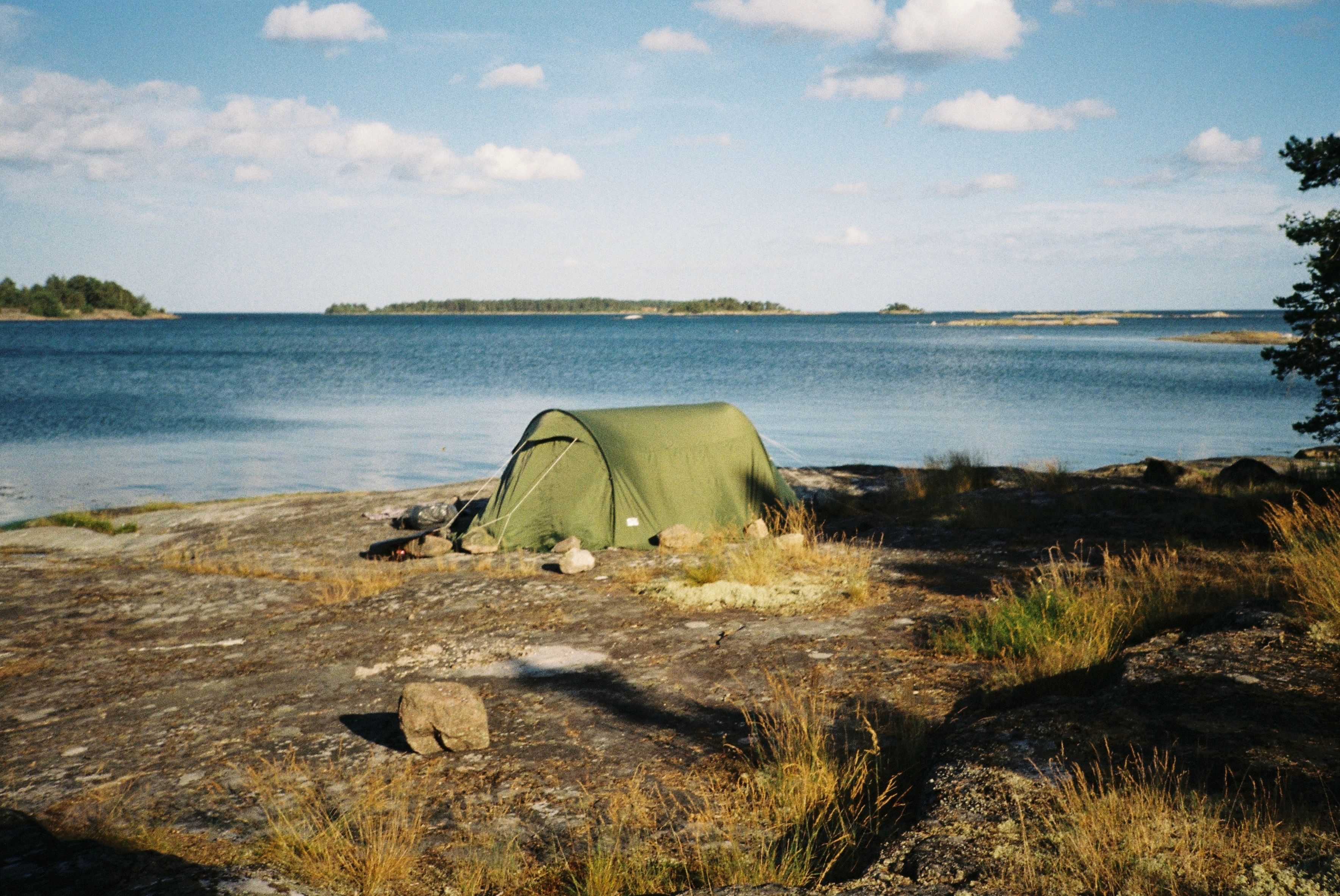 Peaceful green tent on rocky shore by a calm sea, perfect for nature escapes.