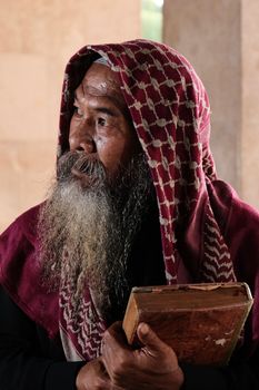 Portrait of an elderly man in traditional attire holding a book, conveying wisdom and contemplation.