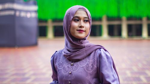 Free Portrait of a young woman in a lavender hijab with a blurred urban outdoor background. Stock Photo