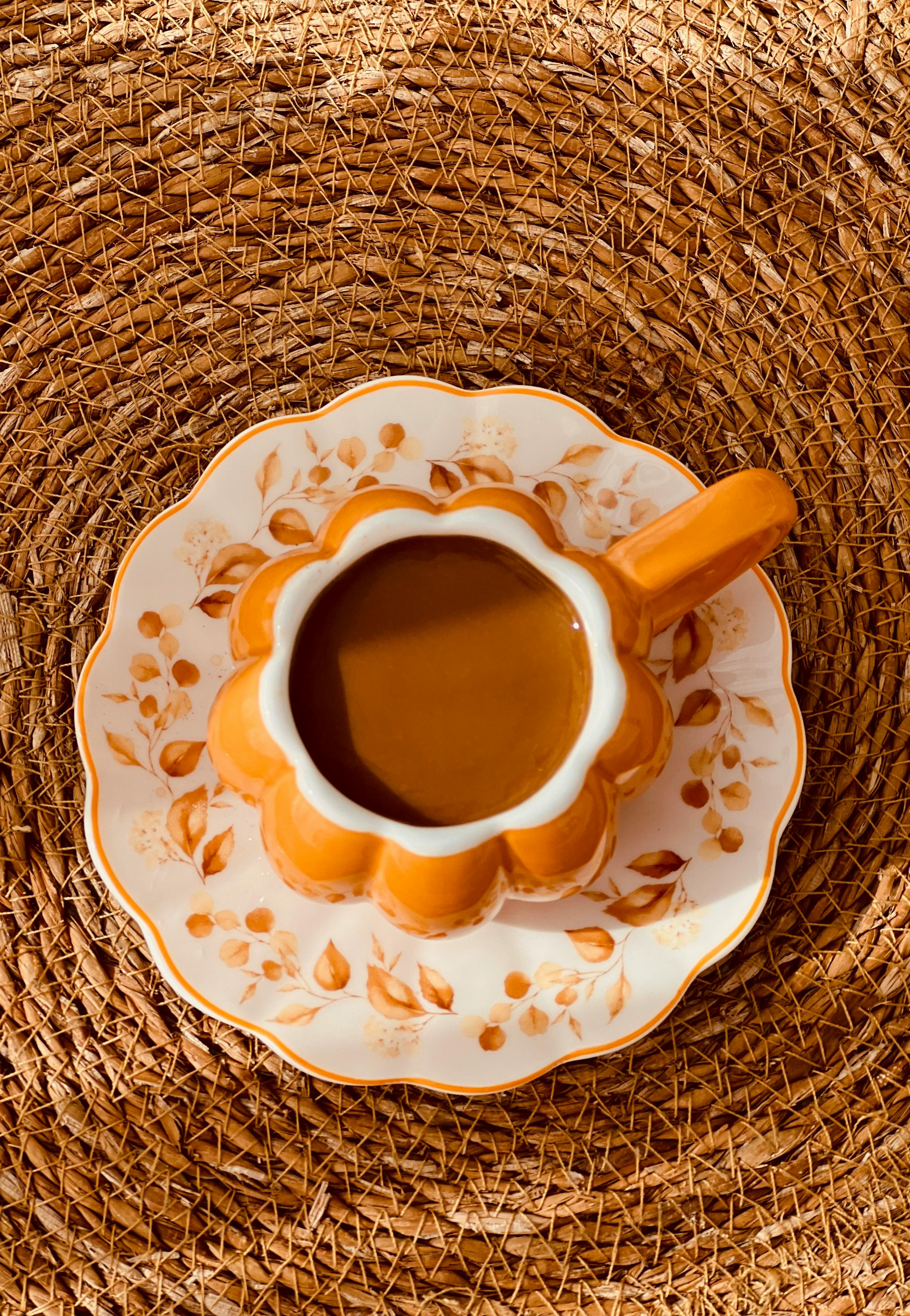 An artistic top view of a pumpkin-shaped coffee cup on a woven mat in autumn.