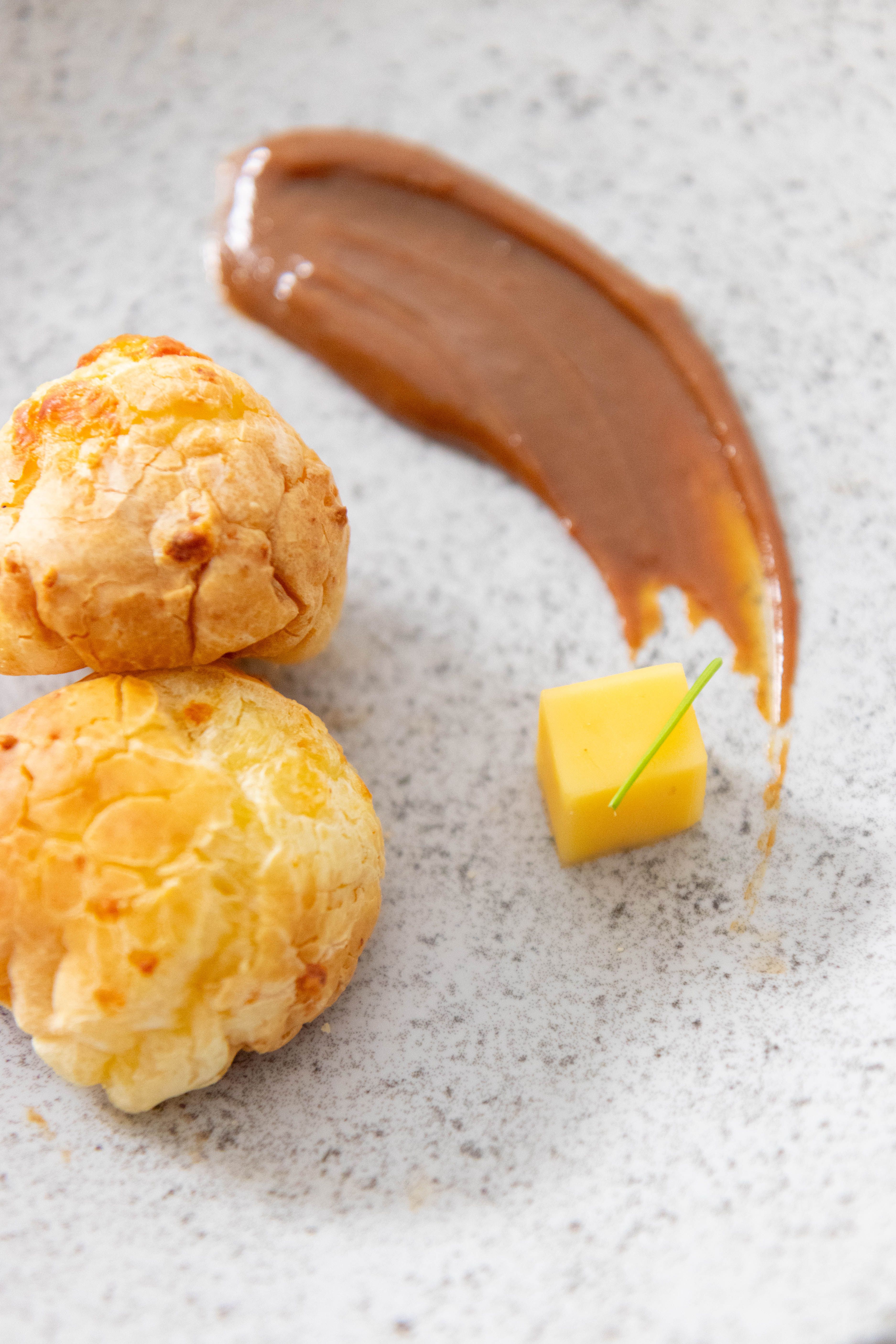 A wooden bowl piled with golden caramel-glazed corn puffs, some broken into small clusters, with a few loose pieces scattered on the counter.
