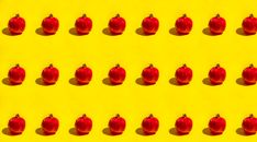 Creative pattern of red pomegranates on a bright yellow background, offering a bold and vibrant fruit-themed design.