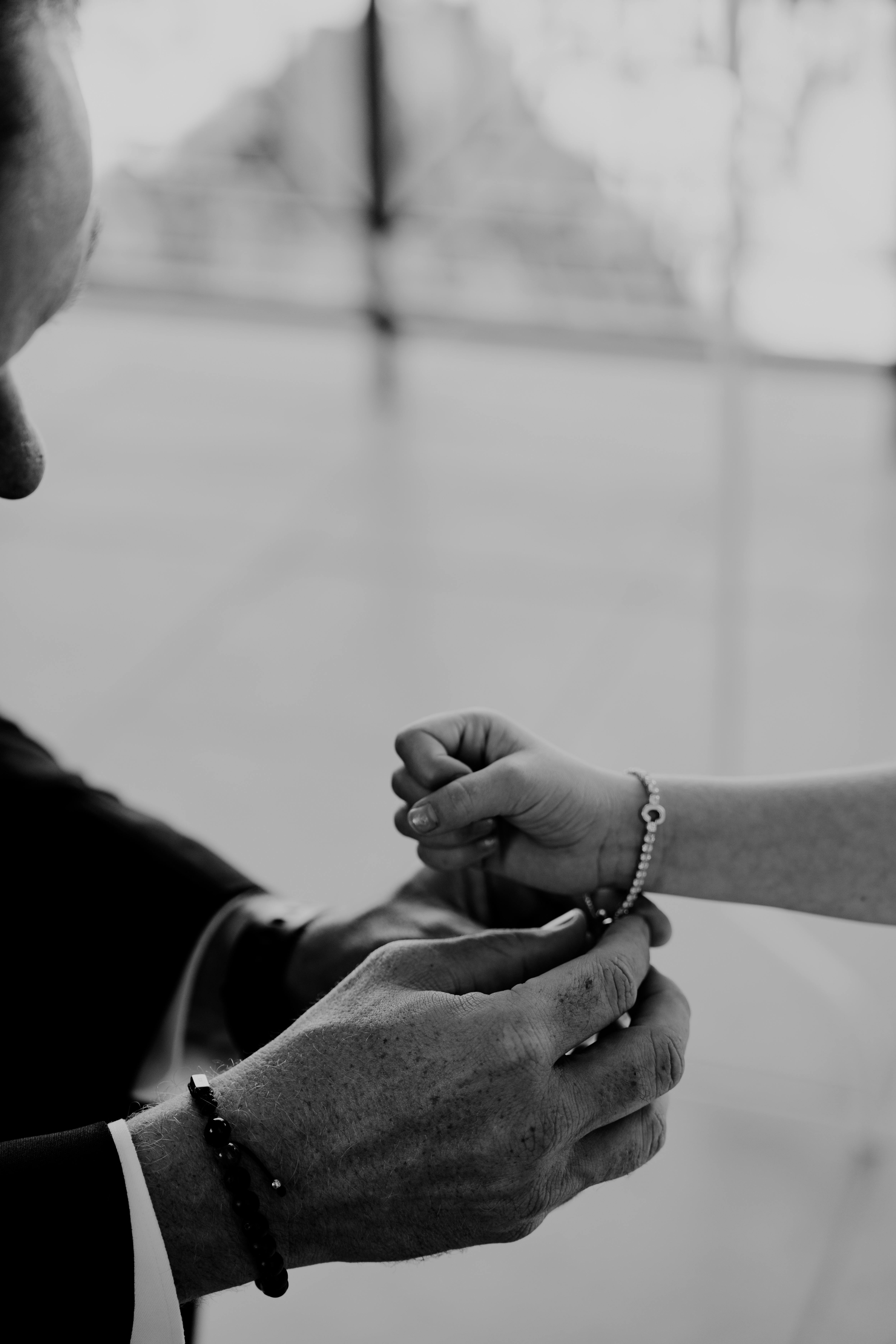 Black and white image capturing a touching bracelet exchange between father and son on a wedding day in Las Vegas.