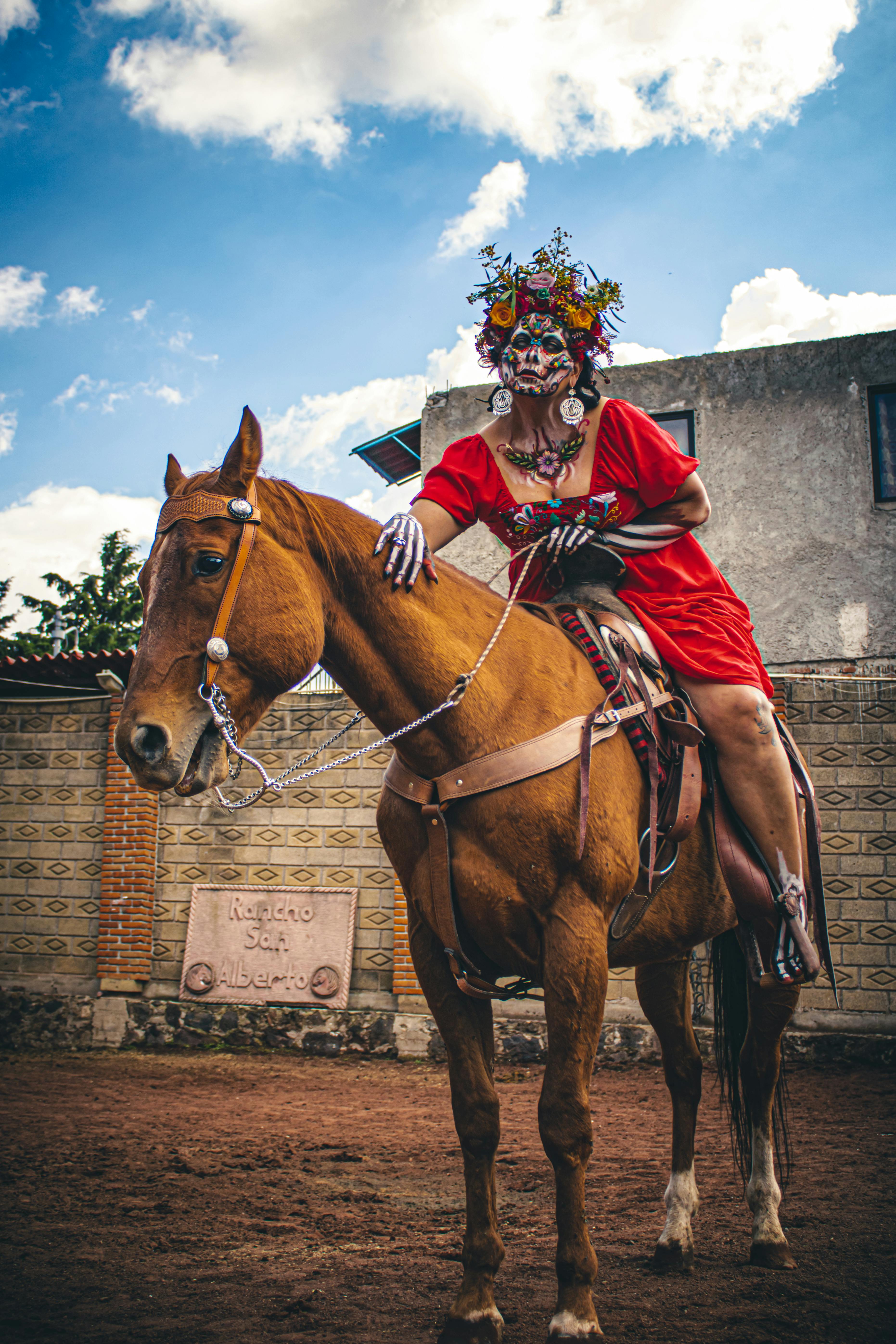 A woman in Catrina makeup and costume sits atop a chestnut horse in Mexico.