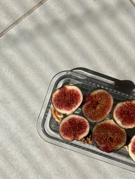 Close-up of sliced figs in sunlight on a glass tray with shadows cast.