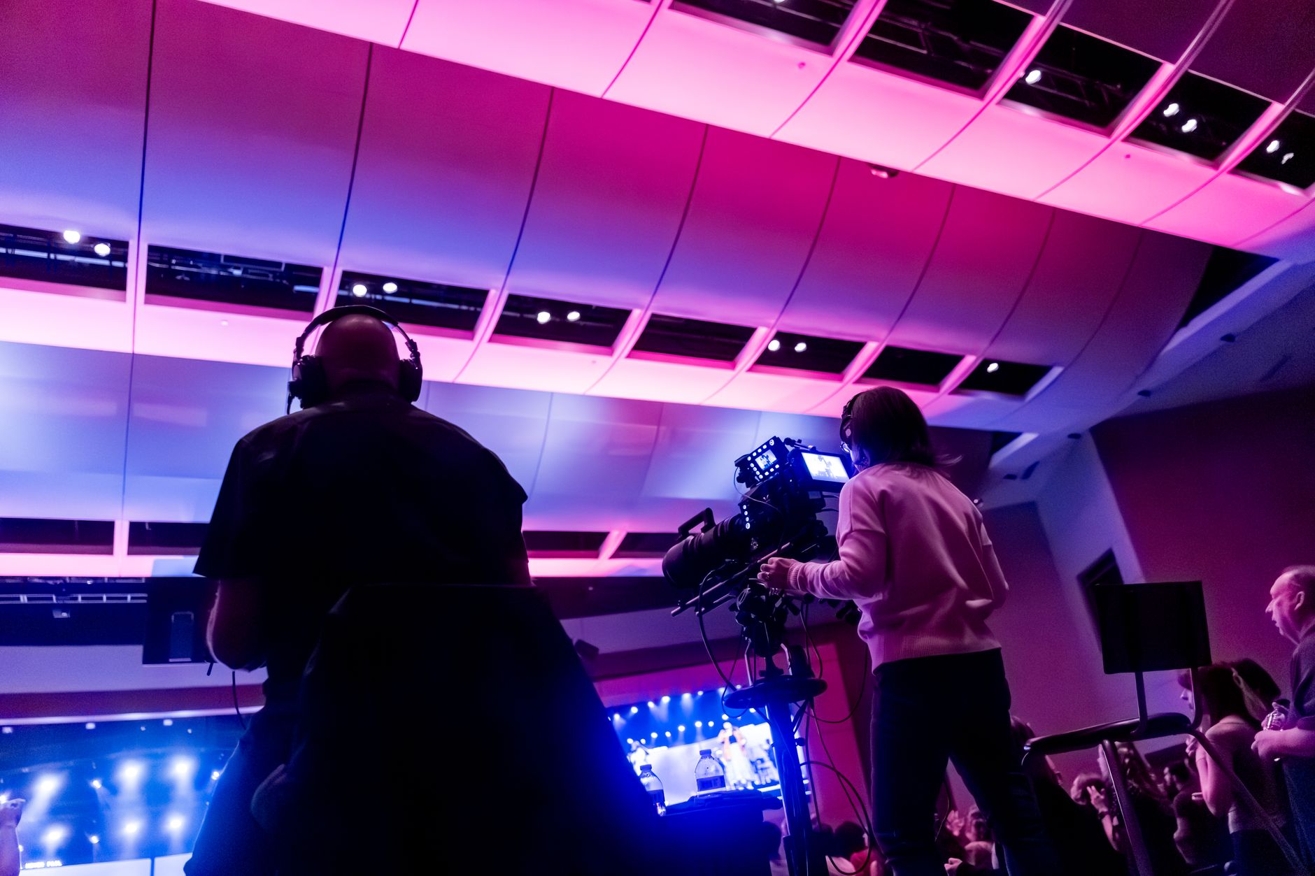 Professional camera crew filming a live event indoors, capturing vibrant stage lighting.
