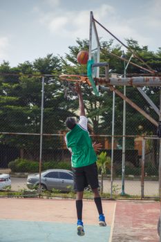 Teenager makes a slam dunk on outdoor basketball court.