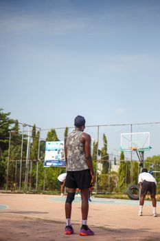 Three young men practice basketball outdoors on a sunny court.