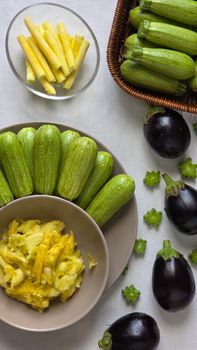 Top-down view of fresh zucchini and eggplants arranged with peeled strips on a white tablecloth.