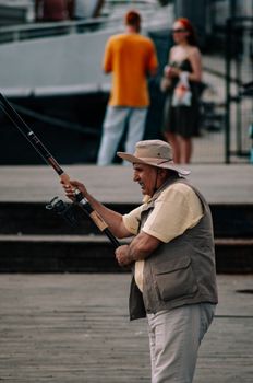 An elderly man fishing with a rod on a pier, capturing a candid urban moment.