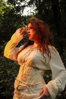 A woman dressed in vintage style using binoculars in a forest setting during sunset.