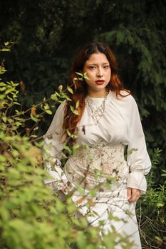 Woman in a vintage outfit surrounded by greenery, showcasing elegance and style.