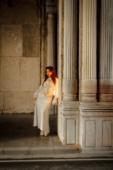 Woman elegantly posing against classic stone columns in soft evening light.