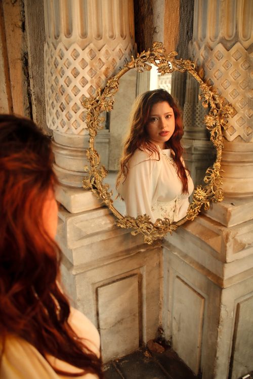 Free A woman gazes into an ornate mirror in a classic architectural setting, creating a vintage and timeless feel. Stock Photo
